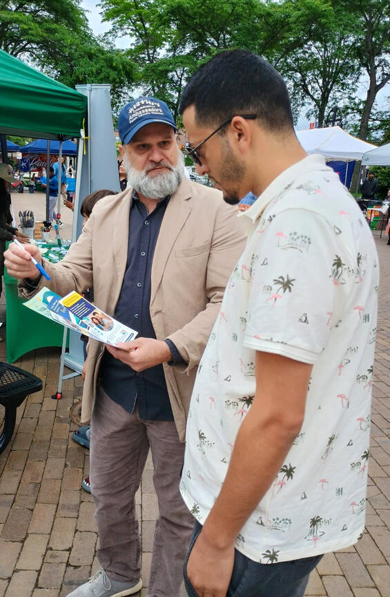 Person wearing a Community Ambassador hat sharing informational flyers with a resident at a community event.