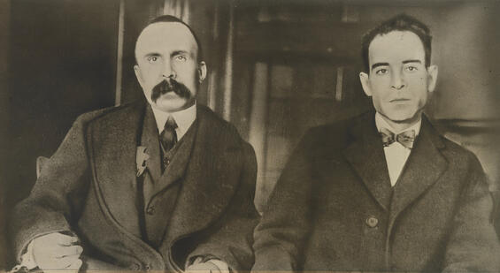 Portait of Nicola Sacco and Bartolomeo Vanzetti sitting in suits with very serious faces 