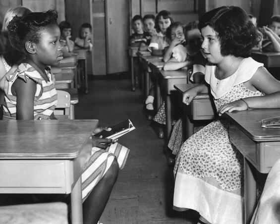 Desegregated school classroom with two young girls of different races looking at each other