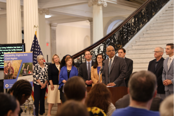 Secretary Mahaniah speaks from a podium at the Grand Staircase on the Community Living Initiative