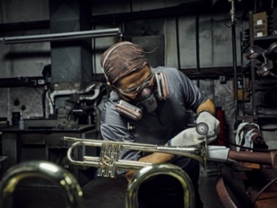 A worker wearing a respirator, safety glasses, and gloves while working on a trumpet at S.E. Shires Company.