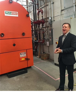 Mark Richey speaking beside a large woodworking machine in a workshop.