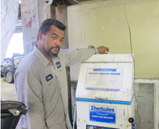 Larry Dossantos, owner of 912 Auto Center, stands next to a blue-and-white Herkules paint gun washer in an auto body shop.