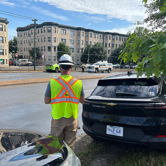 DPU in a yellow and orange safety vest watches MBTA tow a car from the tracks.