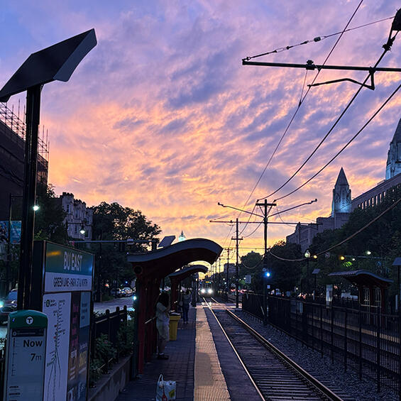 A Green Line train approaches under a purple and orange sunset.