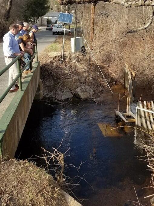 People at a river's edge watching an electronic fish counter.