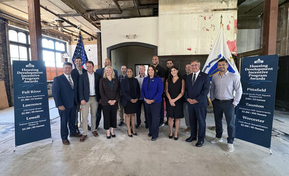 Healey-Driscoll Administration officials stand with representatives of communities receiving HDIP awards in an old mill building