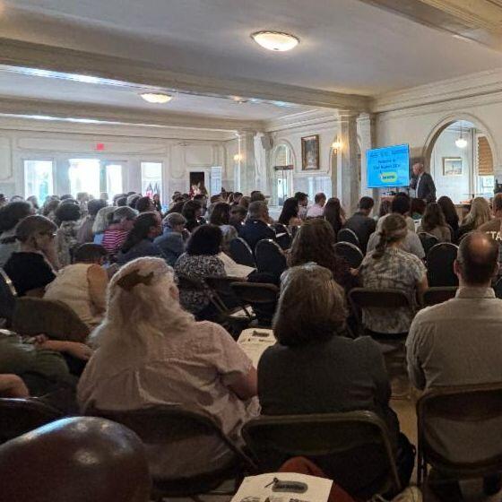 An audience in a large conference room listening to a speaker.
