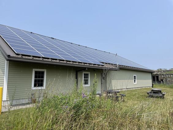 A solar array atop a building roof with a grassy meadow in the foreground