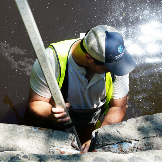View from above a person standing in water and holding a measuring stick.