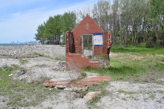 An abandoned brick building stands on a forested island with the City of Boston in the distant background