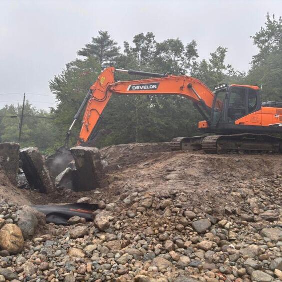 An excavator tearing down a concrete dam.