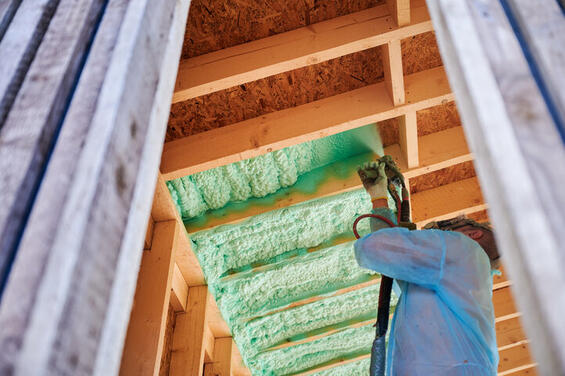 Man in suit spraying insulation into ceiling of home.