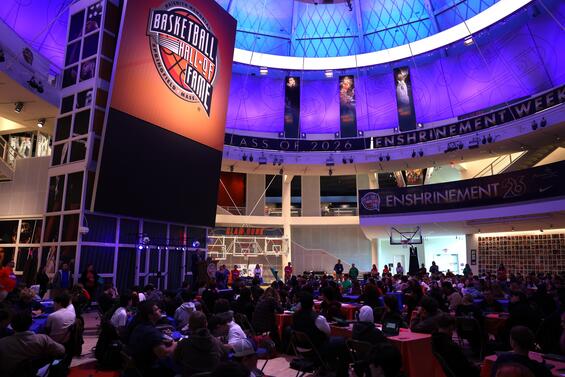 Hundreds of Massachusetts high school students sit in an auditorium inside the Springfield Basketball Hall of Fame. The HOF logo is visible above a large stage and blue and purple lights fill the rotunda's ceiling. 