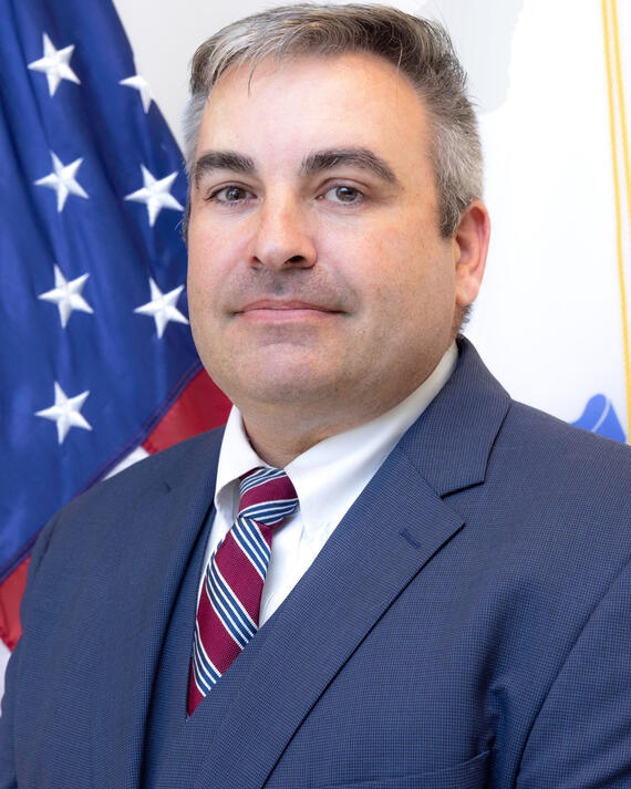 Headshot of Scott Pitta to the right of the United States flag