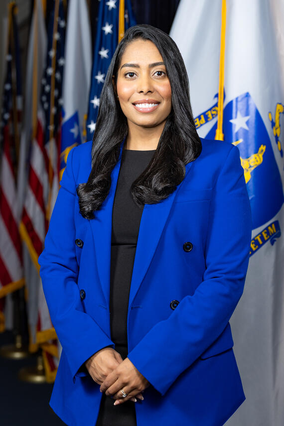 Secretary Juana Matias poses in front of a U.S. and Massachusetts flag for her official portrat