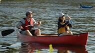 A man and woman canoeing across a quiet pond.