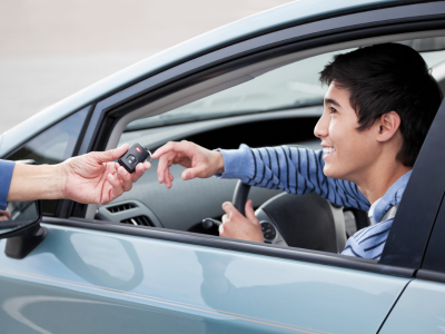 Smiling teen is handed car keys as he sits in a vehicle's driver's seat