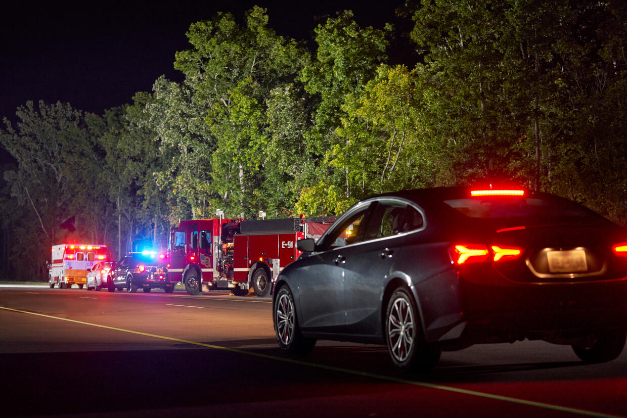 A car passes emergency vehicles on the roadside, making sure to move over a lane to give safe passing distance