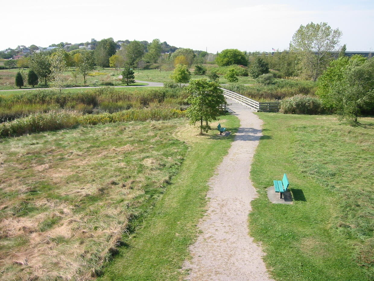 A stone dust trail with a wooden bridge in a flat, grassy meadow.