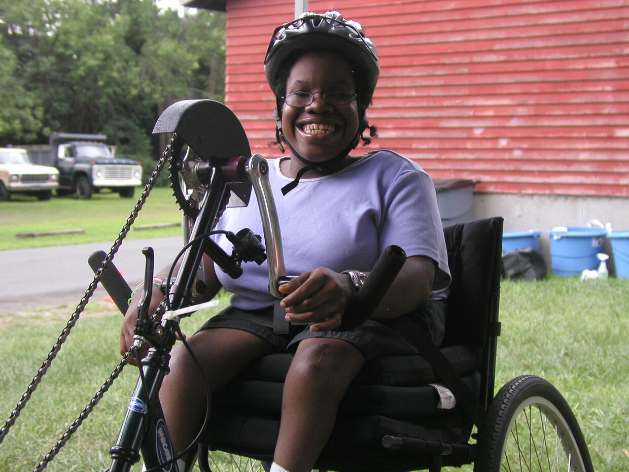 A person wearing a helmet is using a handcycle and smiling at the camera.