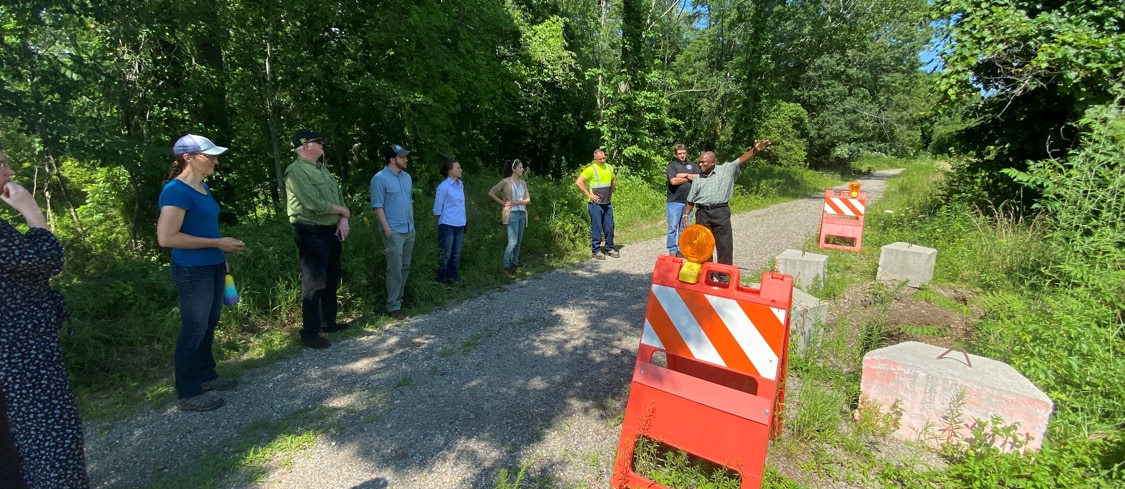 A group of people standing near a culvert with one person speaking and gesturing to the group.