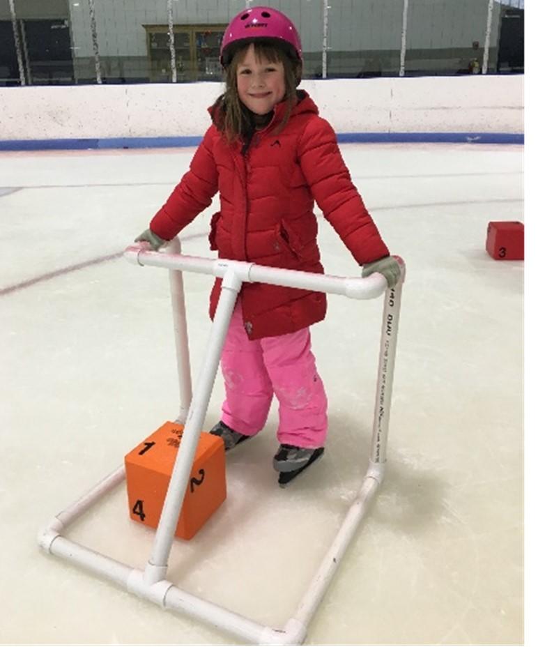 A child ice skating using a walker made of pvc pipe on an ice skating rink.