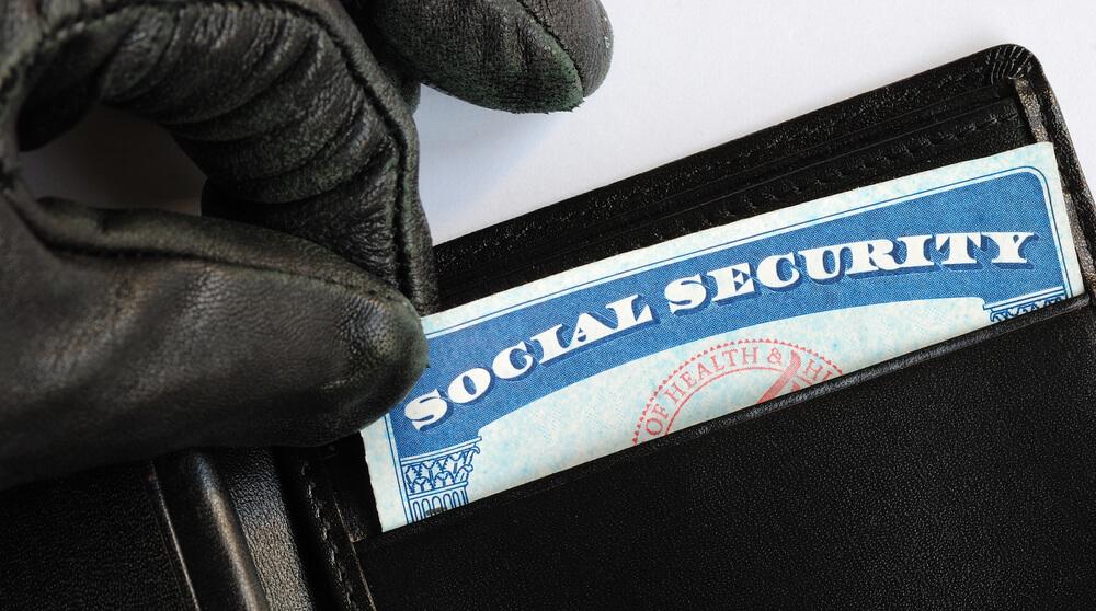 A photo of a gloved hand lifting a social security card from a wallet.