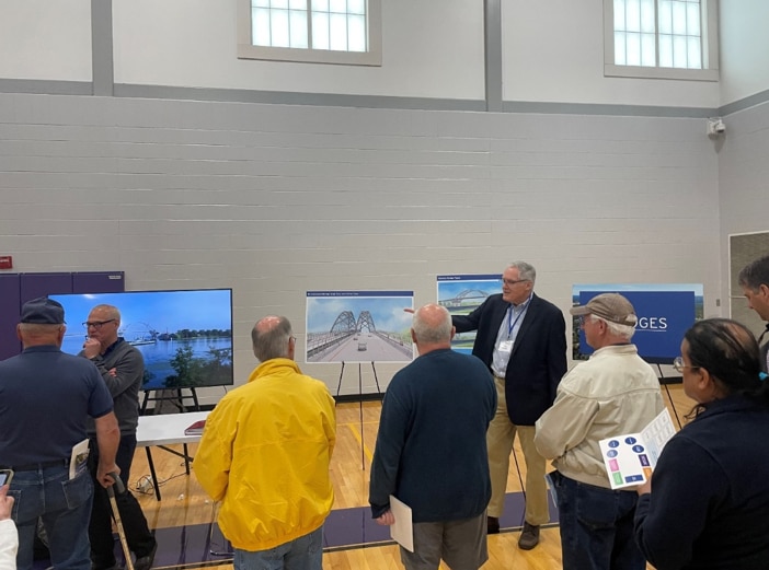 Members of the public gather around a presenter showing Cape Cod Bridges drawings on an easel.