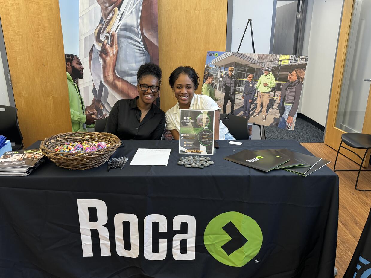 Two staff members from ROCA at the job fair with a table of brochures and giveaways.