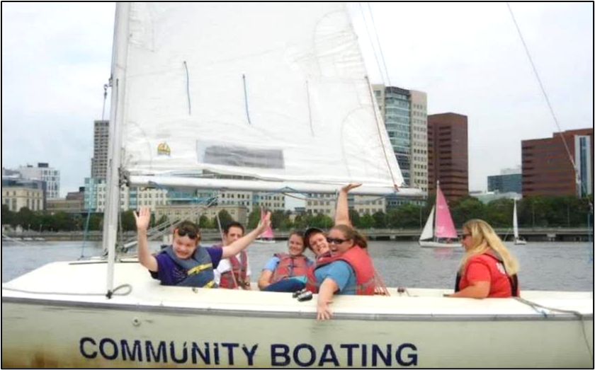A group of people in a sailboat on the river are smiling and waving at the camera. 