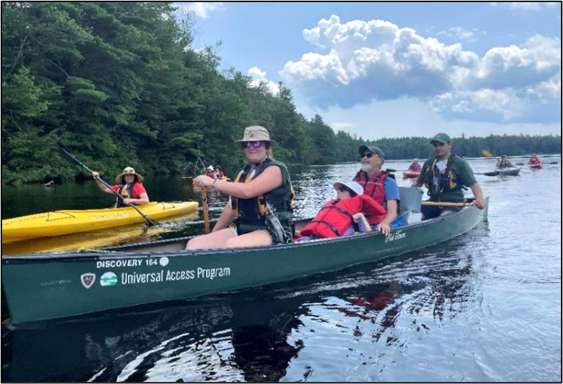 A group of people paddling on a lake.  Some are in canoes and some are riding kayaks.  