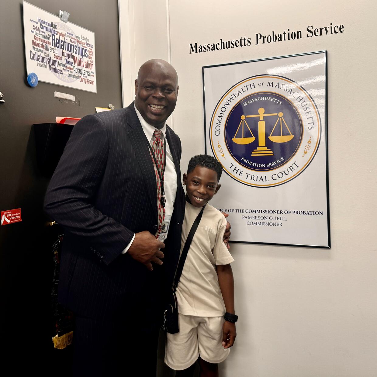 A man and a boy pose for a picture in front of a poster depicting the Massachusetts Trial Court seal. 