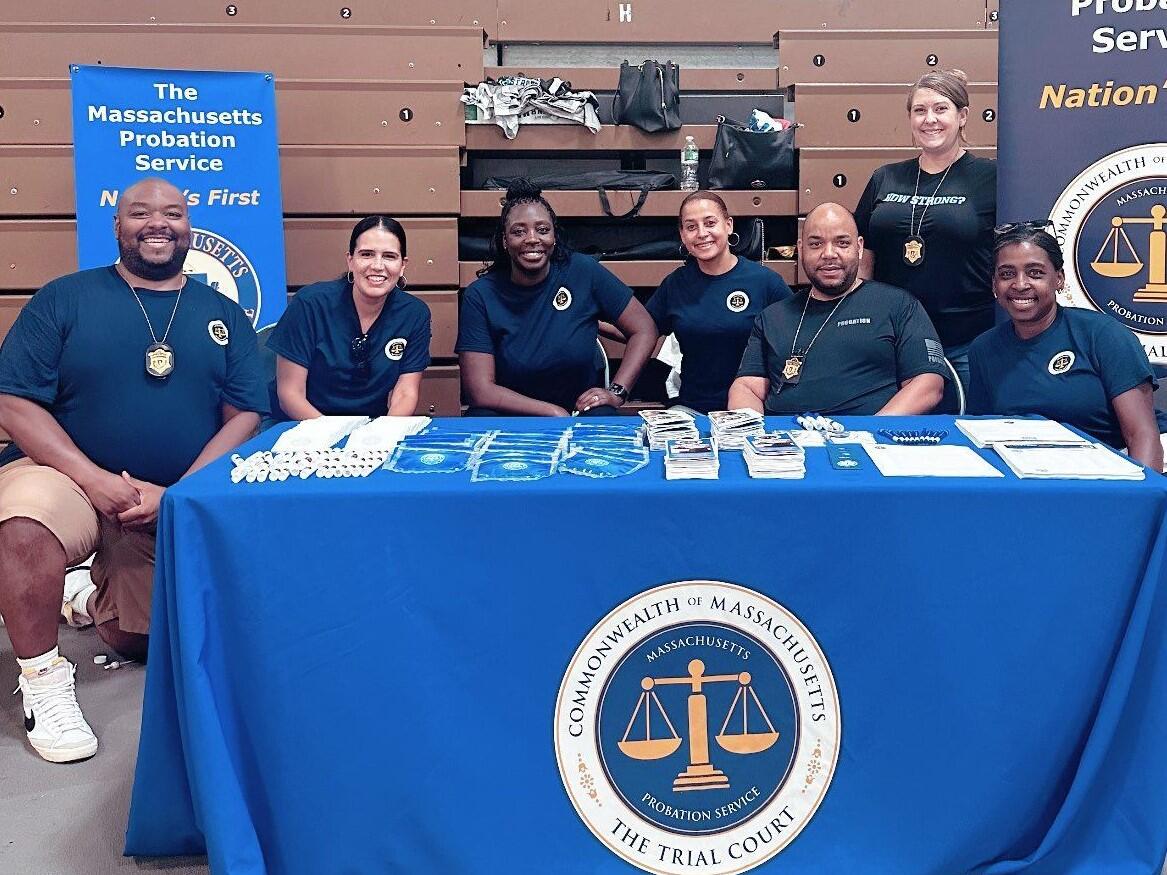 A group of Massachusetts Probation Service (MPS) staff and voluntees sit at a table with the MPS seal