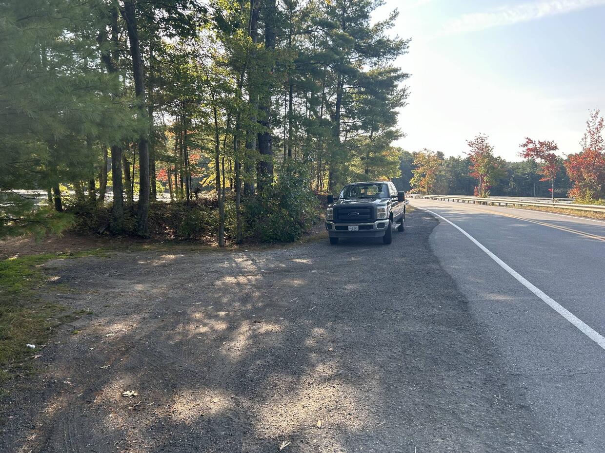 A small, gravel pull-off from the road for parking with one parked car