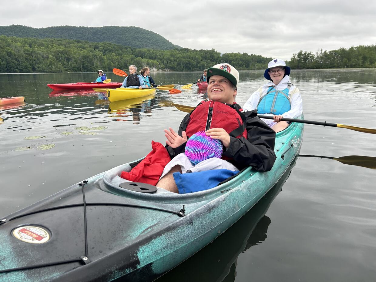 A group of people paddling on a lake.  Some are in canoes and some are riding kayaks.  