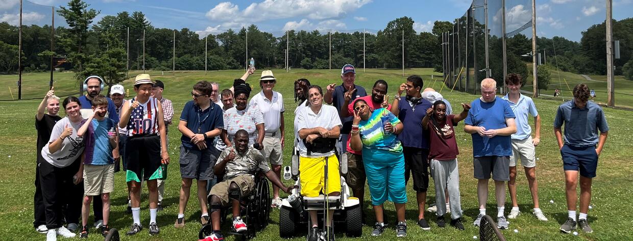 A group of golfers are posing for a photo. One person is using a wheelchair and one person is standing with a para-golfer.