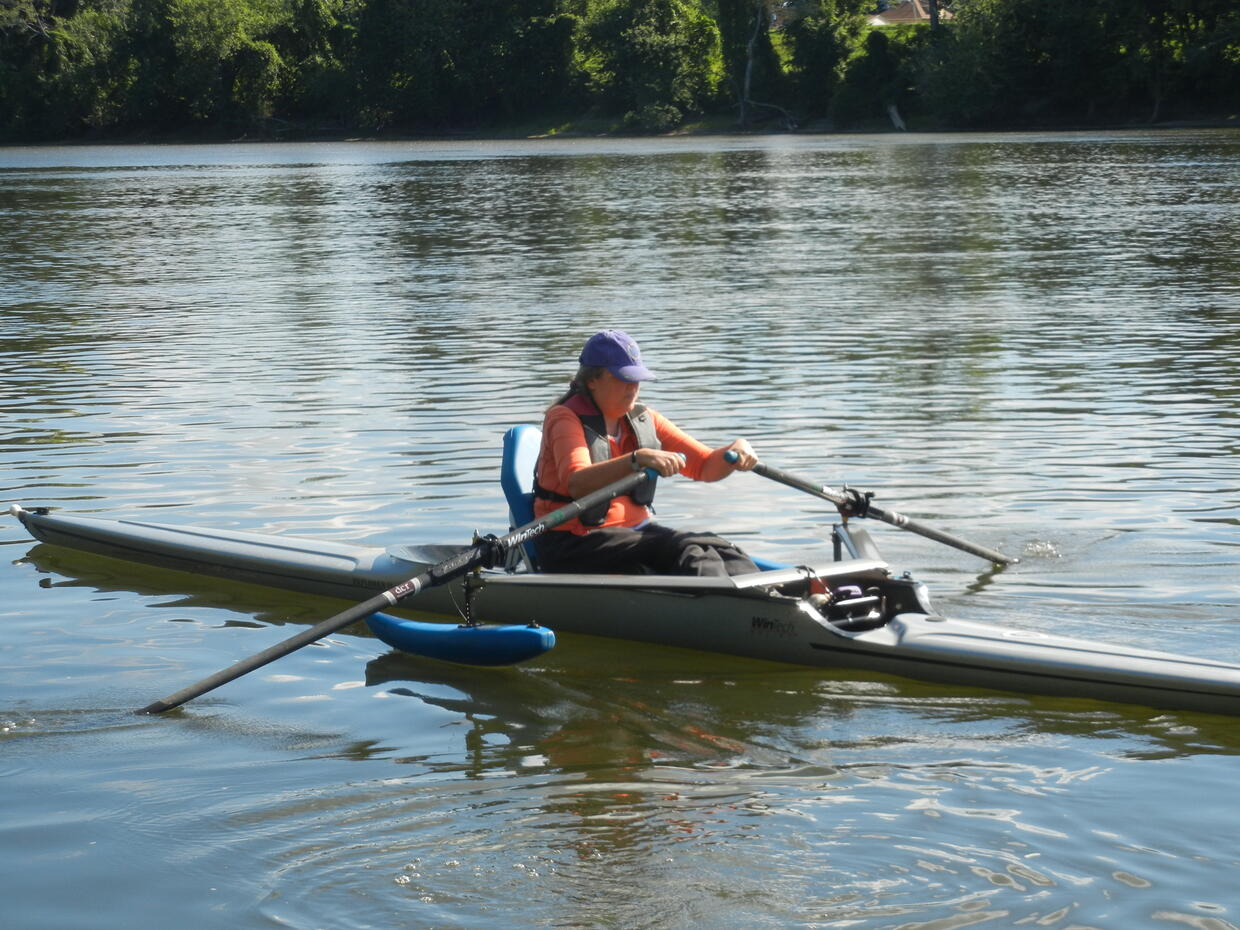 A person is rowing in an boat equipped with outriggers and an adaptive seat. 