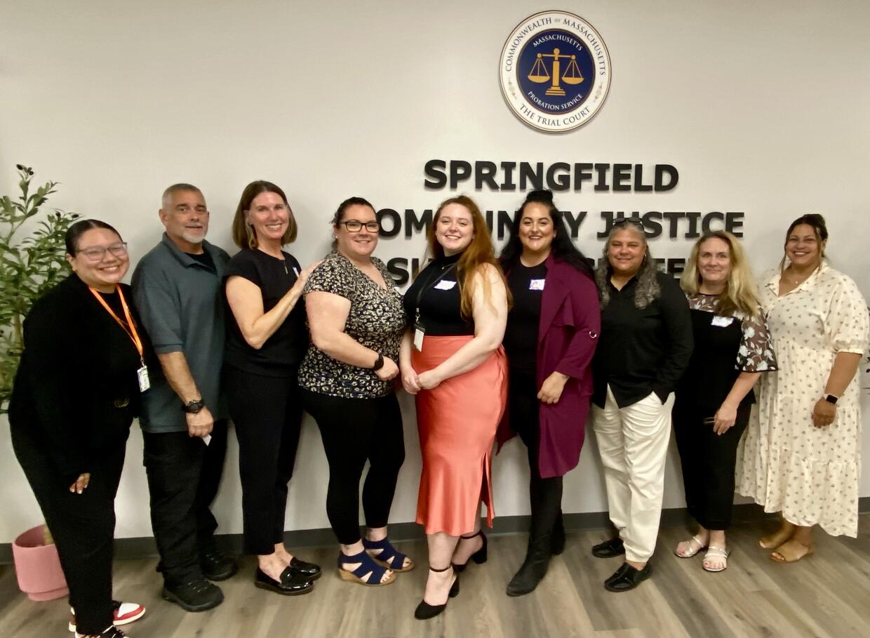  A group of nine adults standing in front of a wall with a logo and text "SPRINGFIELD COMMUNITY JUSTICE."