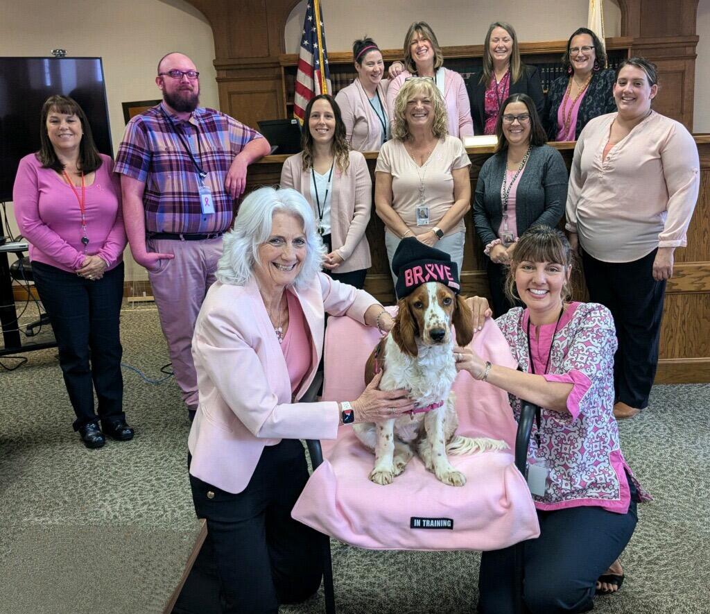 A group of people and a dog wearing pink pose for a picture.
