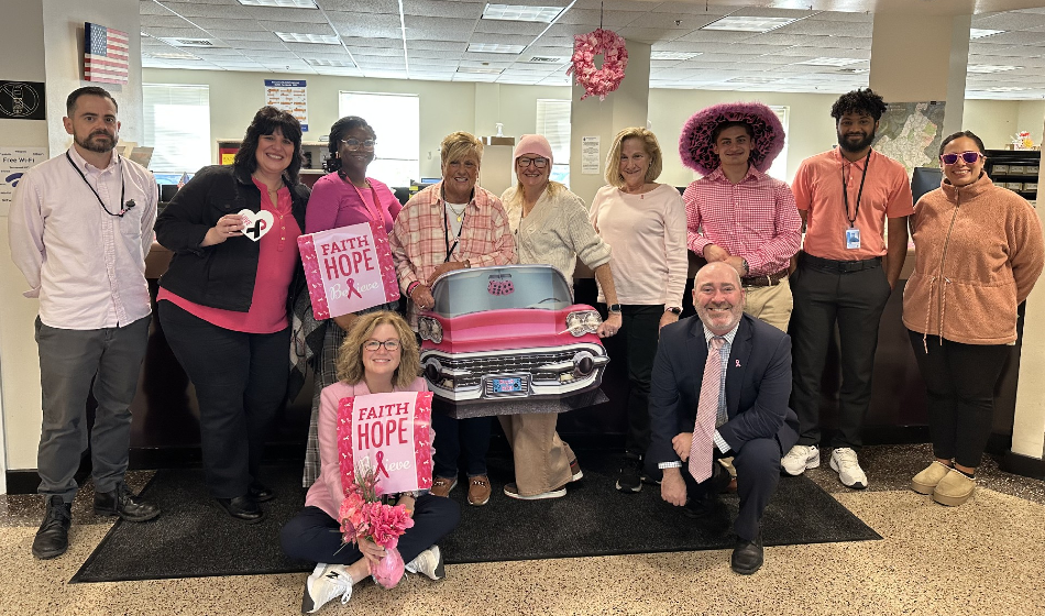 A group of people wearing pink and holding Breast Cancer Awareness posters pose for a picture
