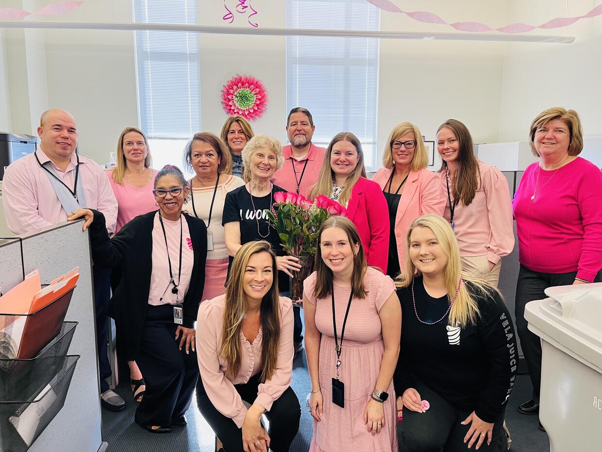 Group of thirteen people in an office dressed in pink