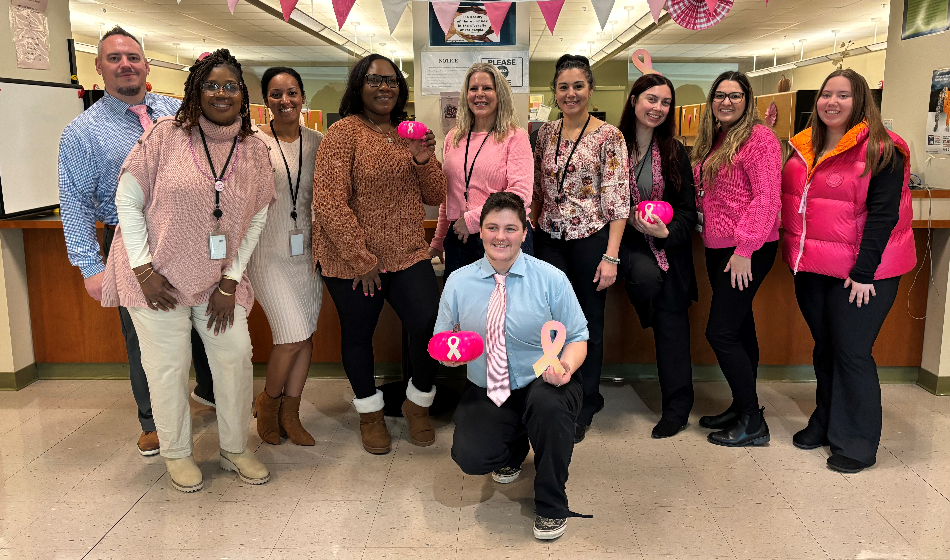 A group of people wearing pink pose in front of an office reception area.