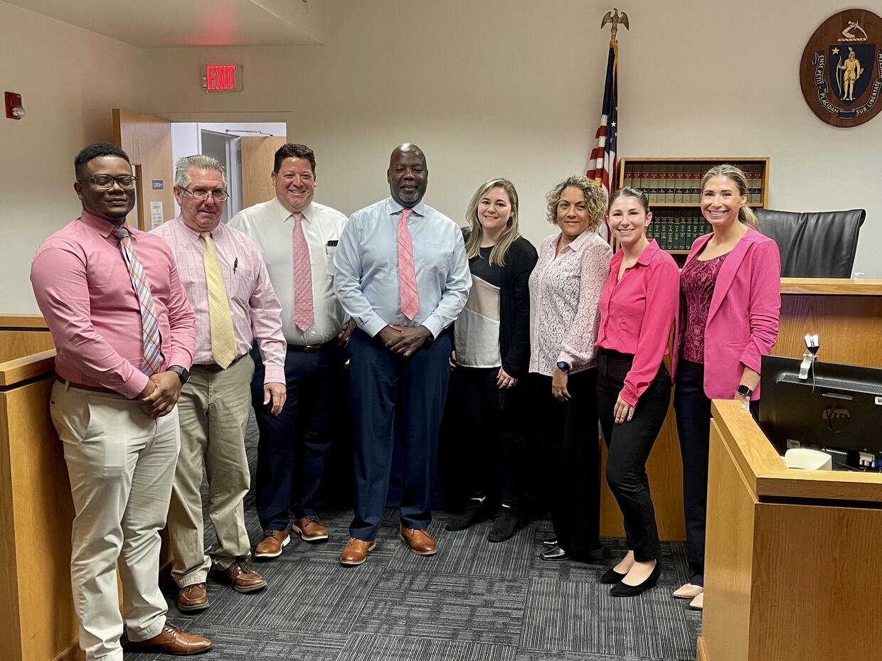 A group of eight people in business attire featuring the color pink standing in a courtroom.