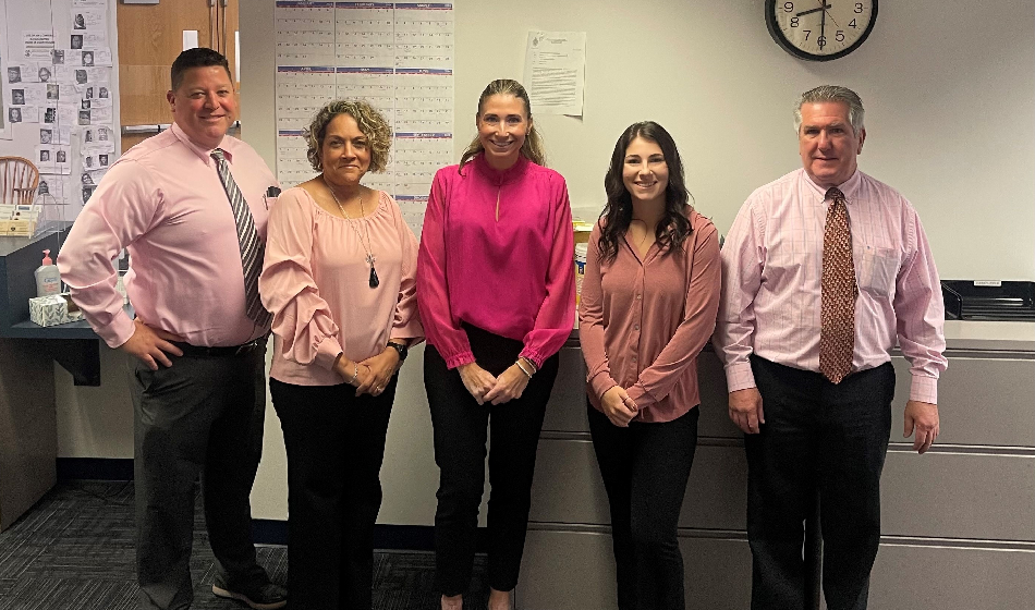 A group of coworkers wearing pink pose for a picture