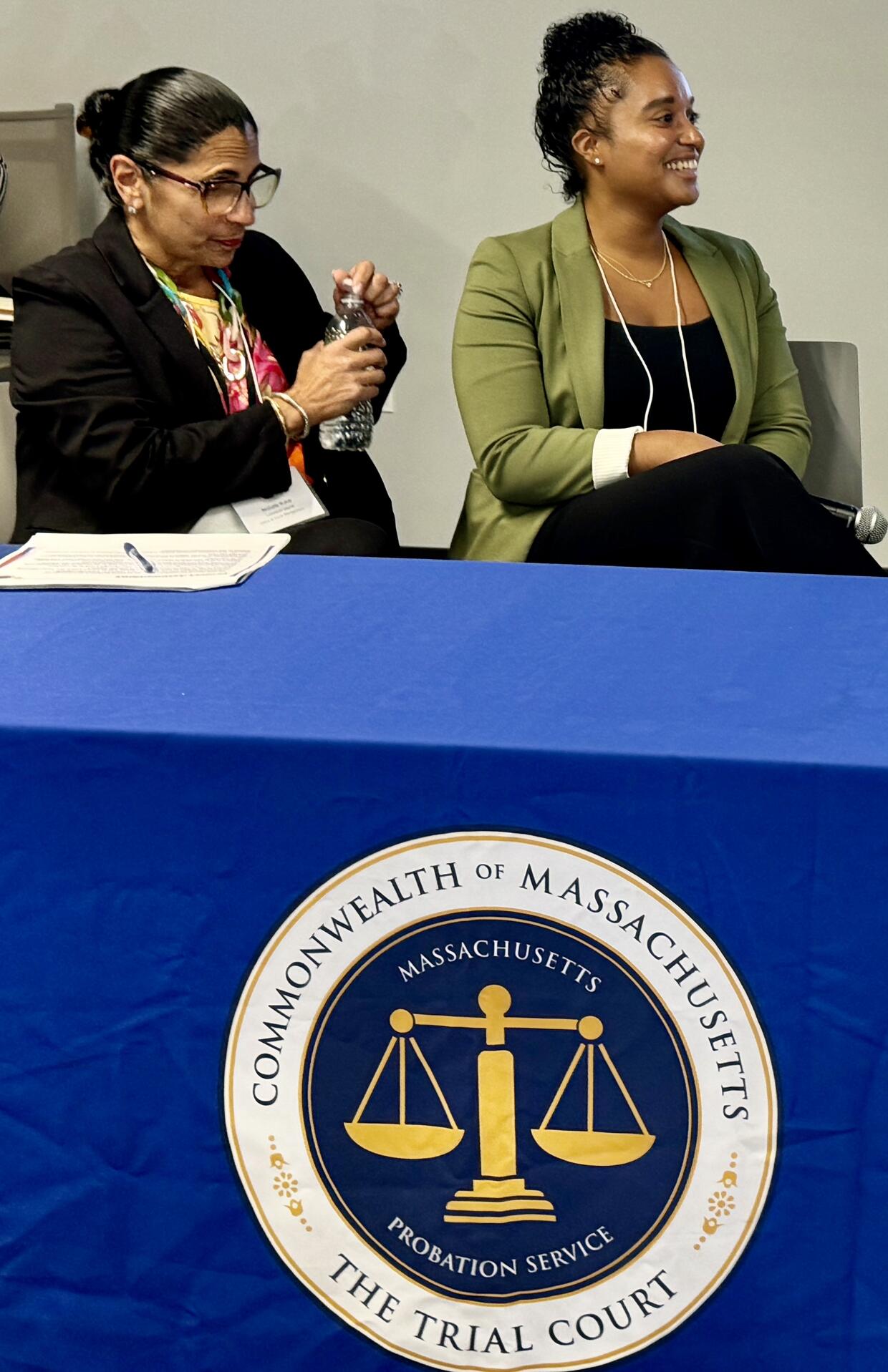 Two women seated behind a blue table with a Massachusetts Trial Court seal.