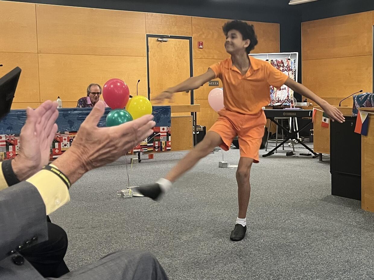 A young man wearing all orange dances for a crowd in a court room.