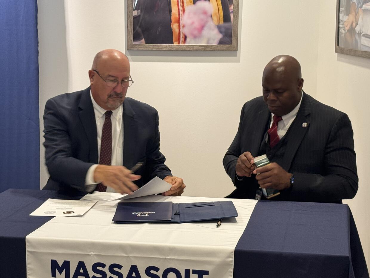 Two men sit at a table with an MOU in between them on a table