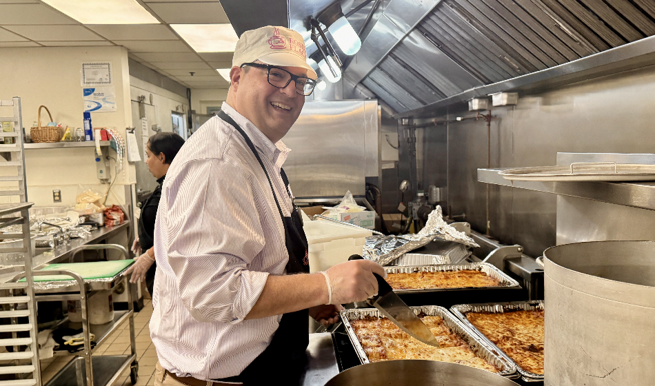 A smiling man cuts into a tray of lasagna.