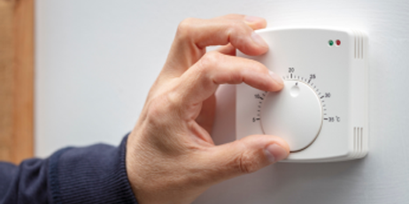 Hand adjusting a central heating thermostat dial